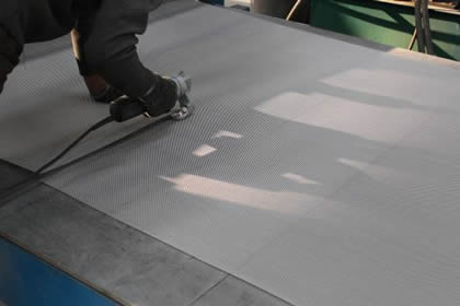 A worker is cutting stainless steel 304 security screen into the required size using specialized cutting equipment.