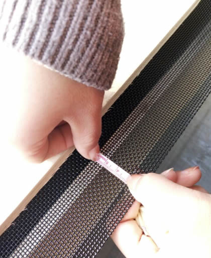 Two hands are measuring the security screen mesh size.